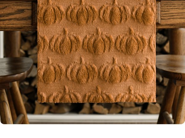 Caramel faux fur table runner with embossed pumpkin pattern draped over a wooden table.