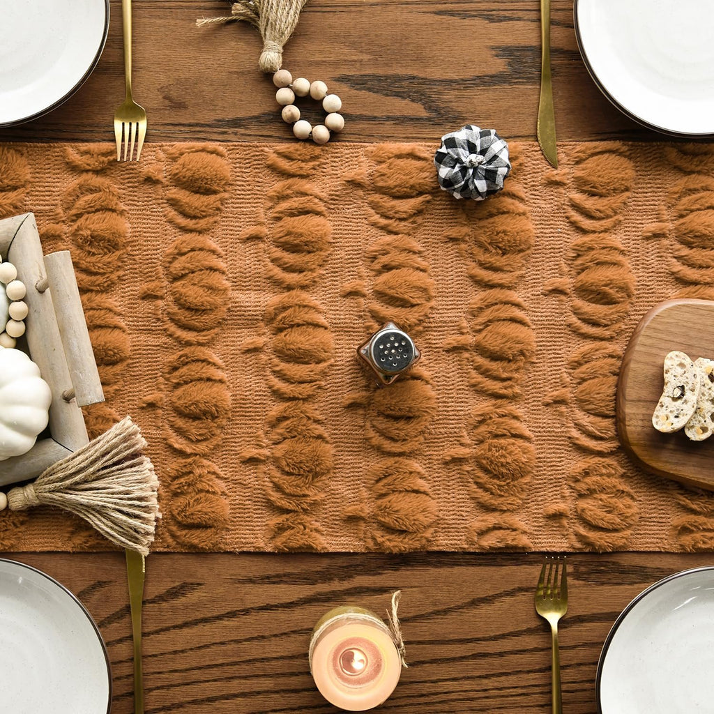 Caramel faux fur table runner with pumpkin pattern on a wooden table set for dining.