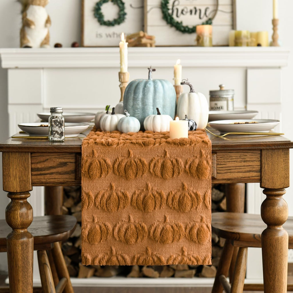 Caramel faux fur pumpkin table runner on a wooden dining table with fall decor, including pumpkins and candles.
