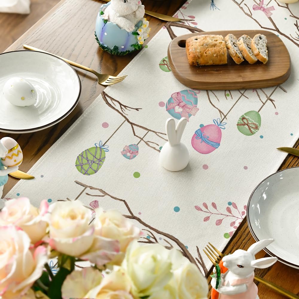 Easter table runner with painted eggs and branches on a dining table setting with plates and bread.