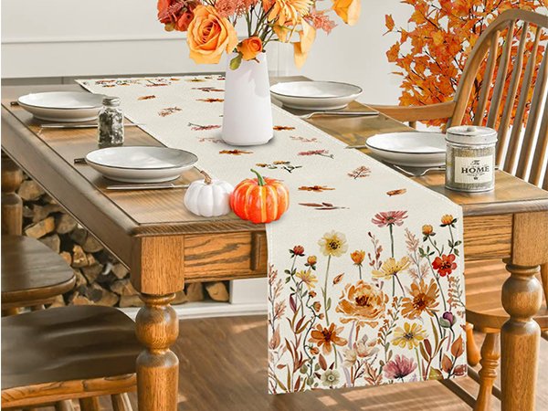 Fall floral table runner with autumn leaves and flowers set on a dining table with plates and pumpkins