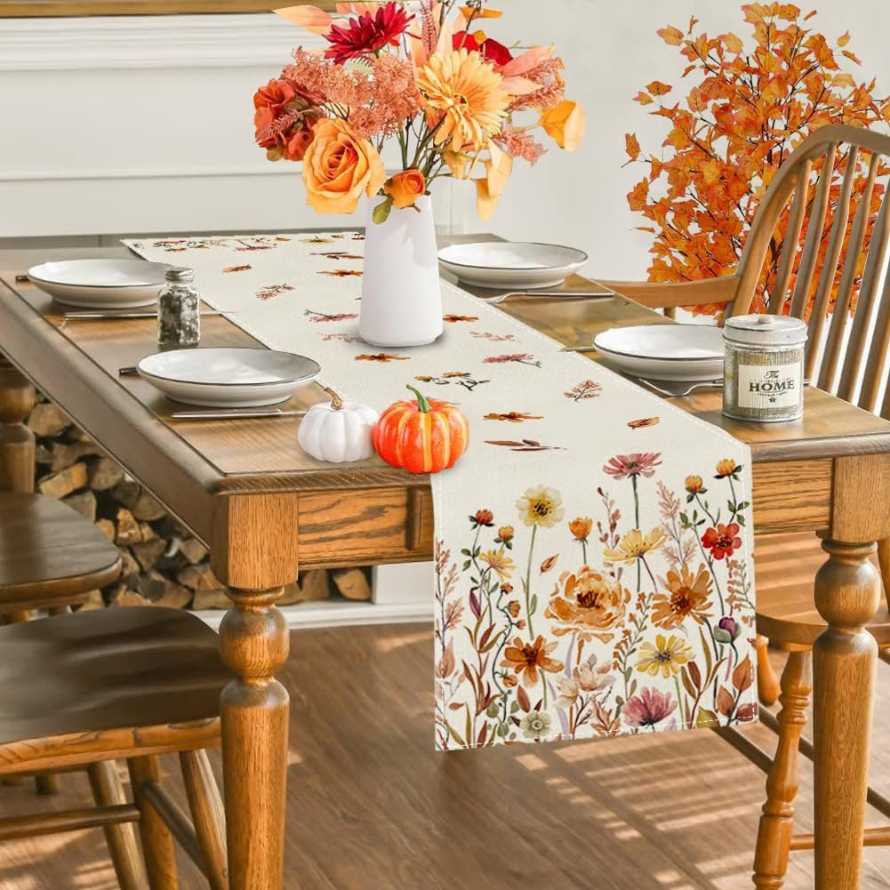 Fall floral table runner with autumn leaves and flowers draped on a wooden dining table with place settings.