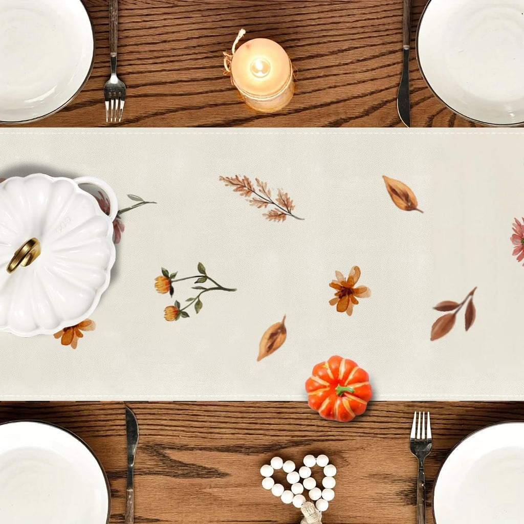 Fall floral table runner with autumn leaves and flowers, set on a dining table with place settings.