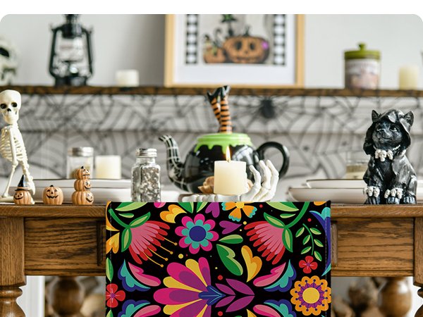 Floral Dia De Los Muertos serape table runner with colorful folk art flowers on a black background, displayed on a wooden table with Halloween decorations.