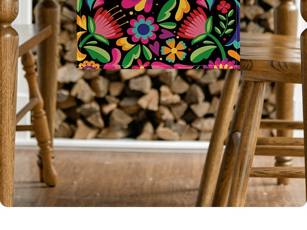 Floral Dia De Los Muertos serape table runner draped over a wooden table with chairs and stacked firewood in the background.