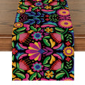Floral Dia De Los Muertos serape table runner on a wooden table, featuring vibrant colors and a black background.