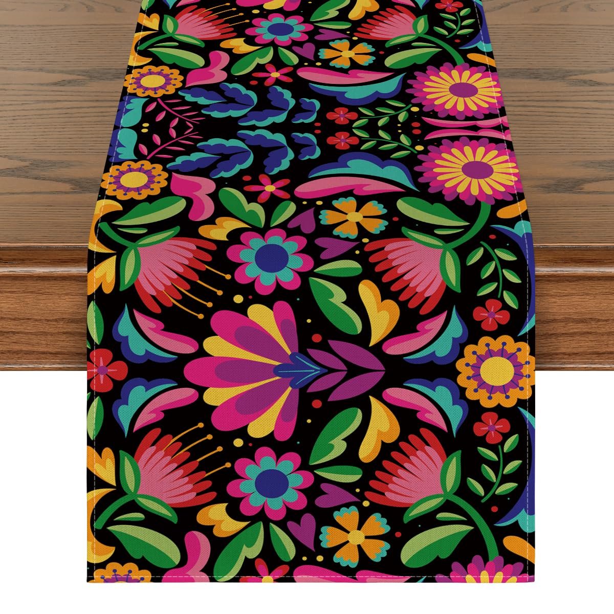 Floral Dia De Los Muertos serape table runner on a wooden table, featuring vibrant colors and a black background.