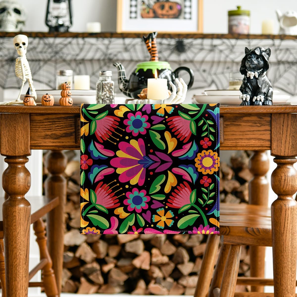 Floral serape table runner with colorful embroidered flowers on a black background, draped over a wooden table with Halloween decorations.