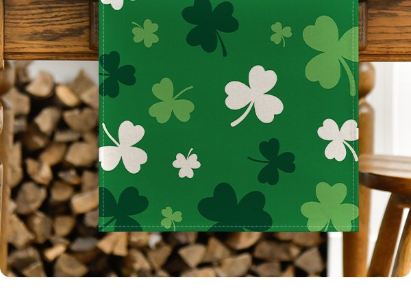 Green St. Patrick's Day table runner with shamrock pattern, draped over wooden furniture near a stack of firewood.