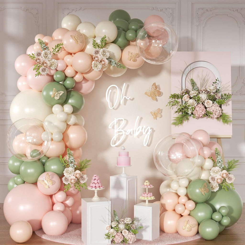 Pink and sage green balloon arch with gold butterflies and floral accents, featuring a neon 'Oh Baby' sign and a tiered cake.