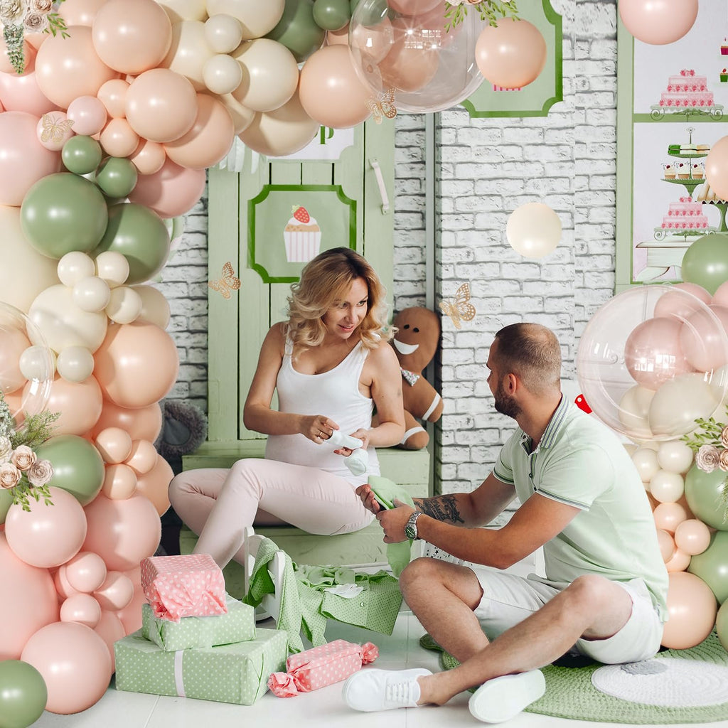 Pregnant woman and man opening gifts surrounded by pink and sage green balloons