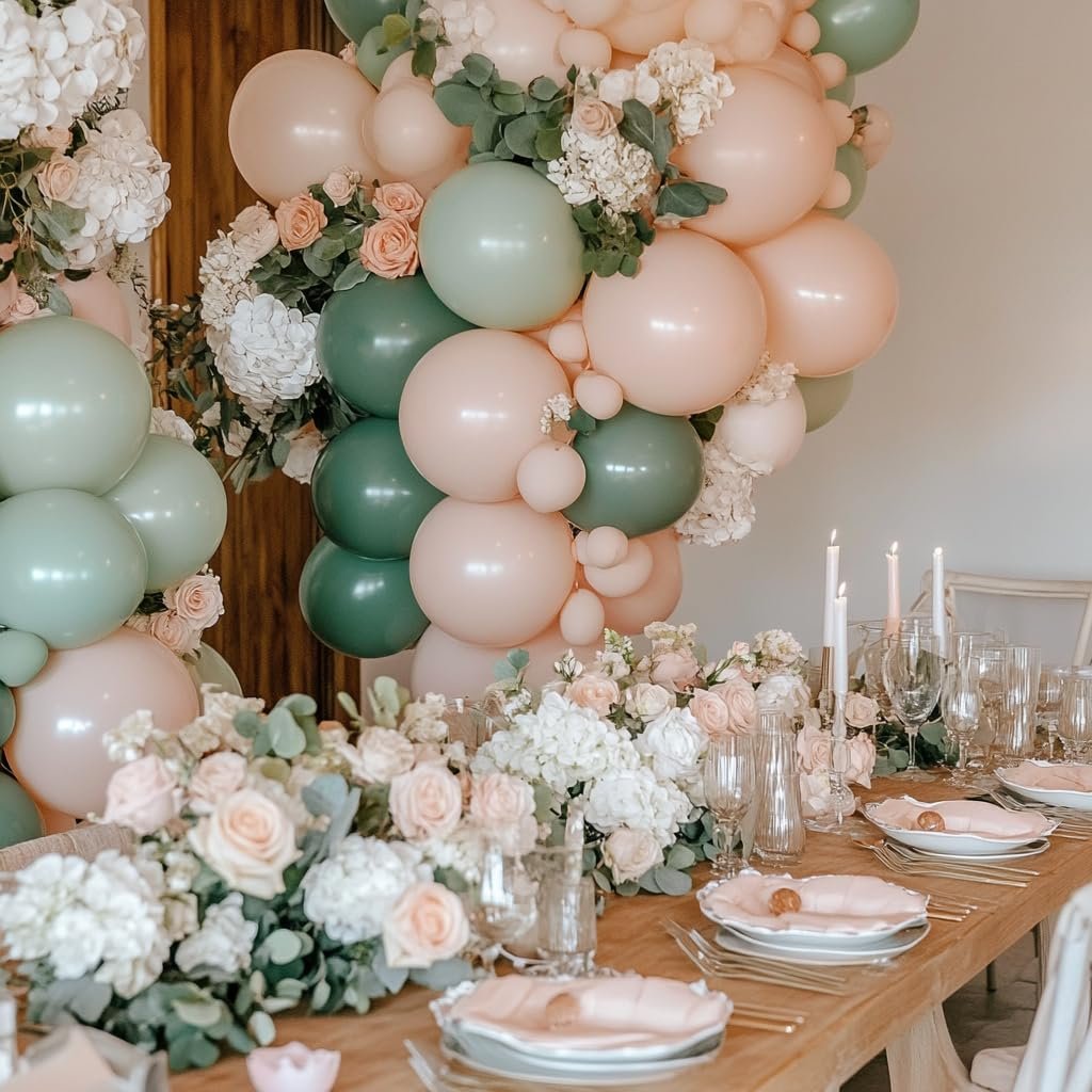 Pink and sage green balloon arch with floral arrangements over a set dining table with candles