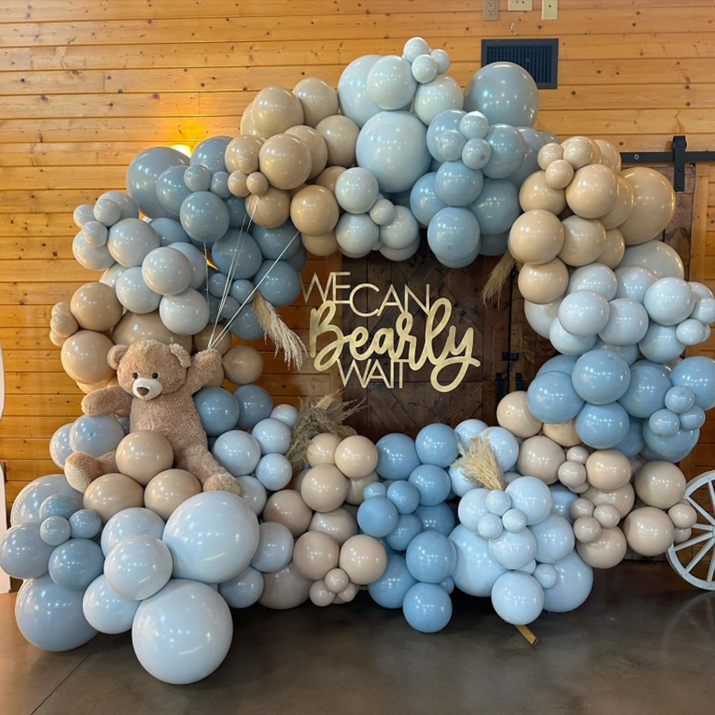 Balloon arch with dusty light baby blue and brown balloons, featuring a teddy bear and a wooden sign that says 'We Can Bearly Wait'.
