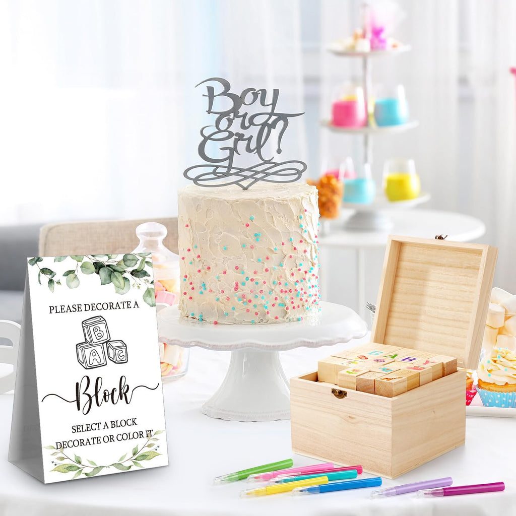Baby shower block decorating game kit with wooden blocks, markers, and sign next to a cake.