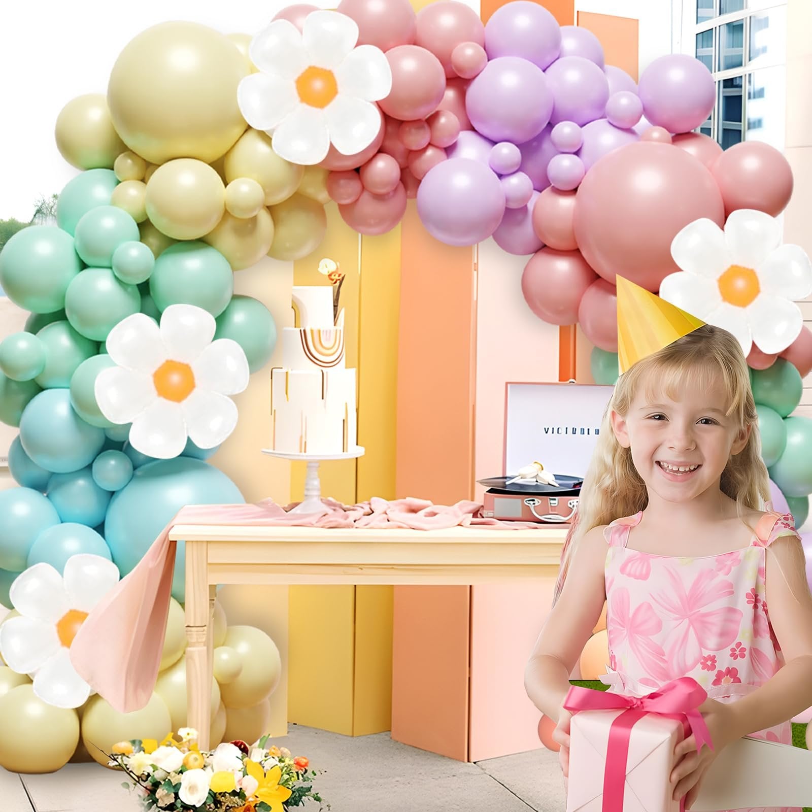 Girl holding a gift in front of a pastel balloon arch and a cake, with a vintage record player on a table.