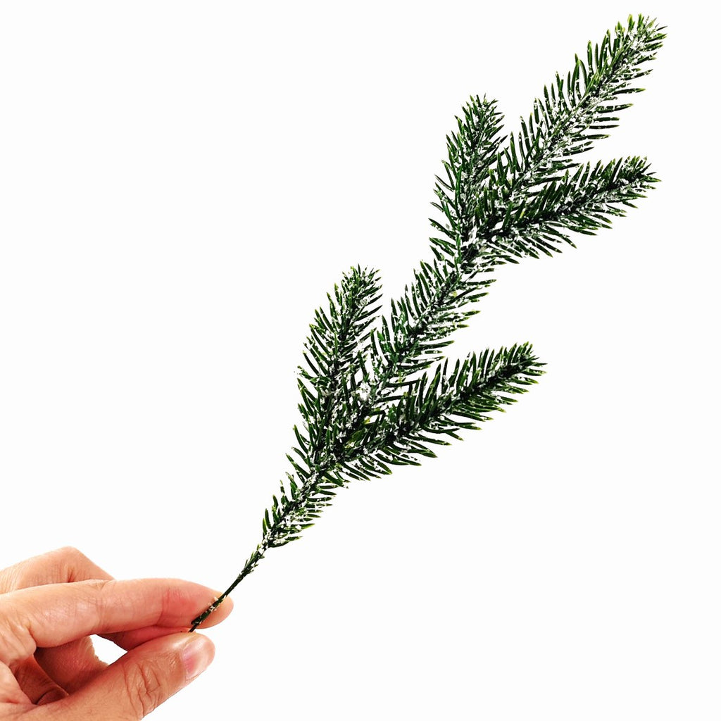 Hand holding a snow-frosted artificial pine branch against a white background