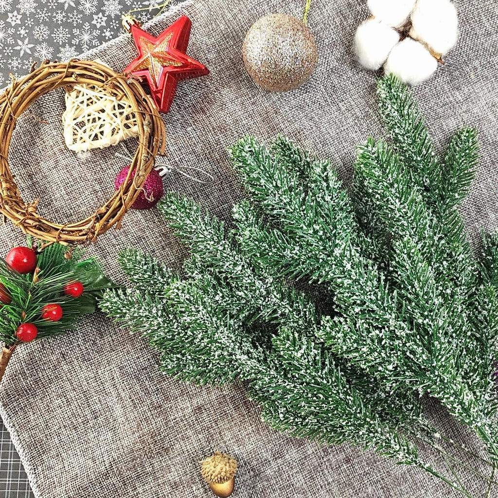 Snow-frosted artificial pine branches with Christmas ornaments and craft supplies on a textured surface