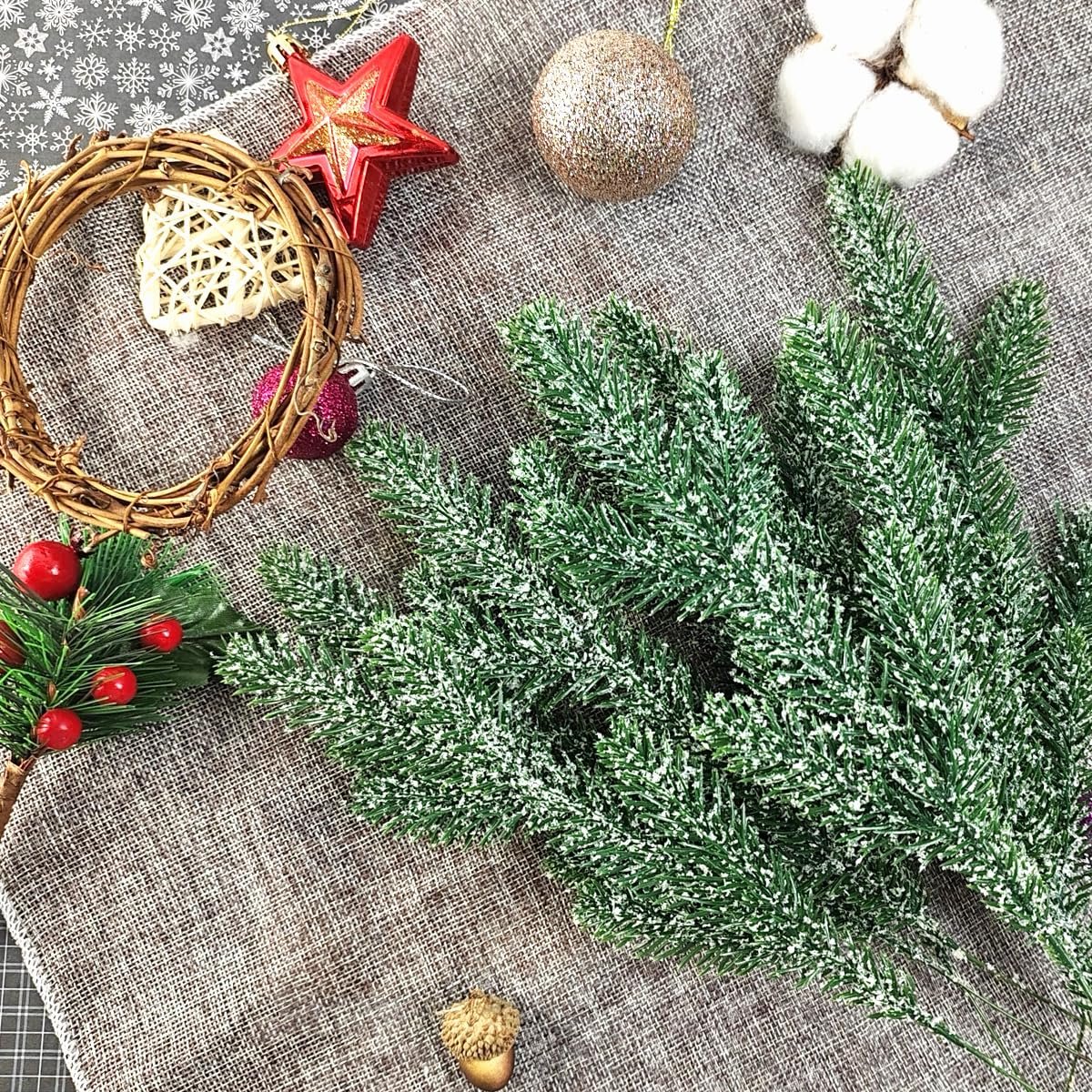 Snow-frosted artificial pine branches with Christmas ornaments and craft supplies on a textured surface