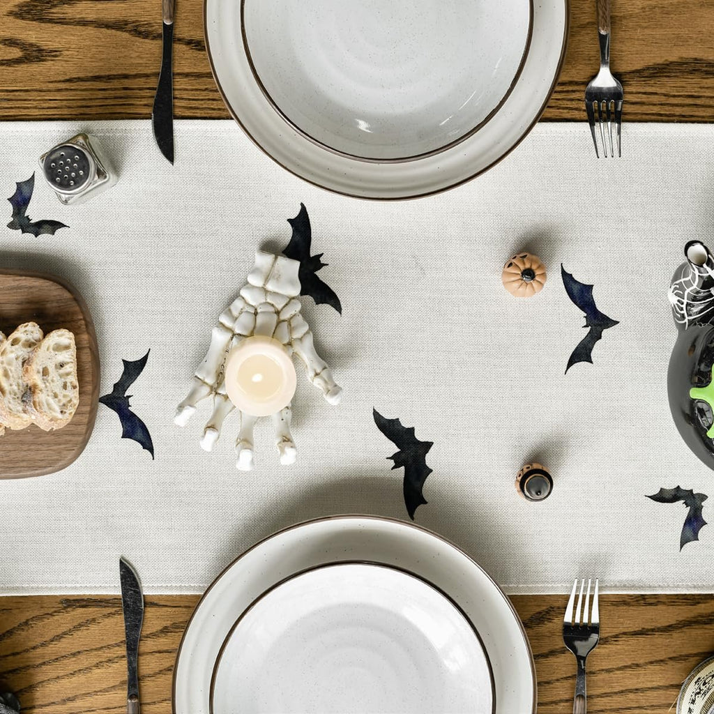 Halloween table setting with a black bat runner, skeleton hand candle holder, plates, and bread.
