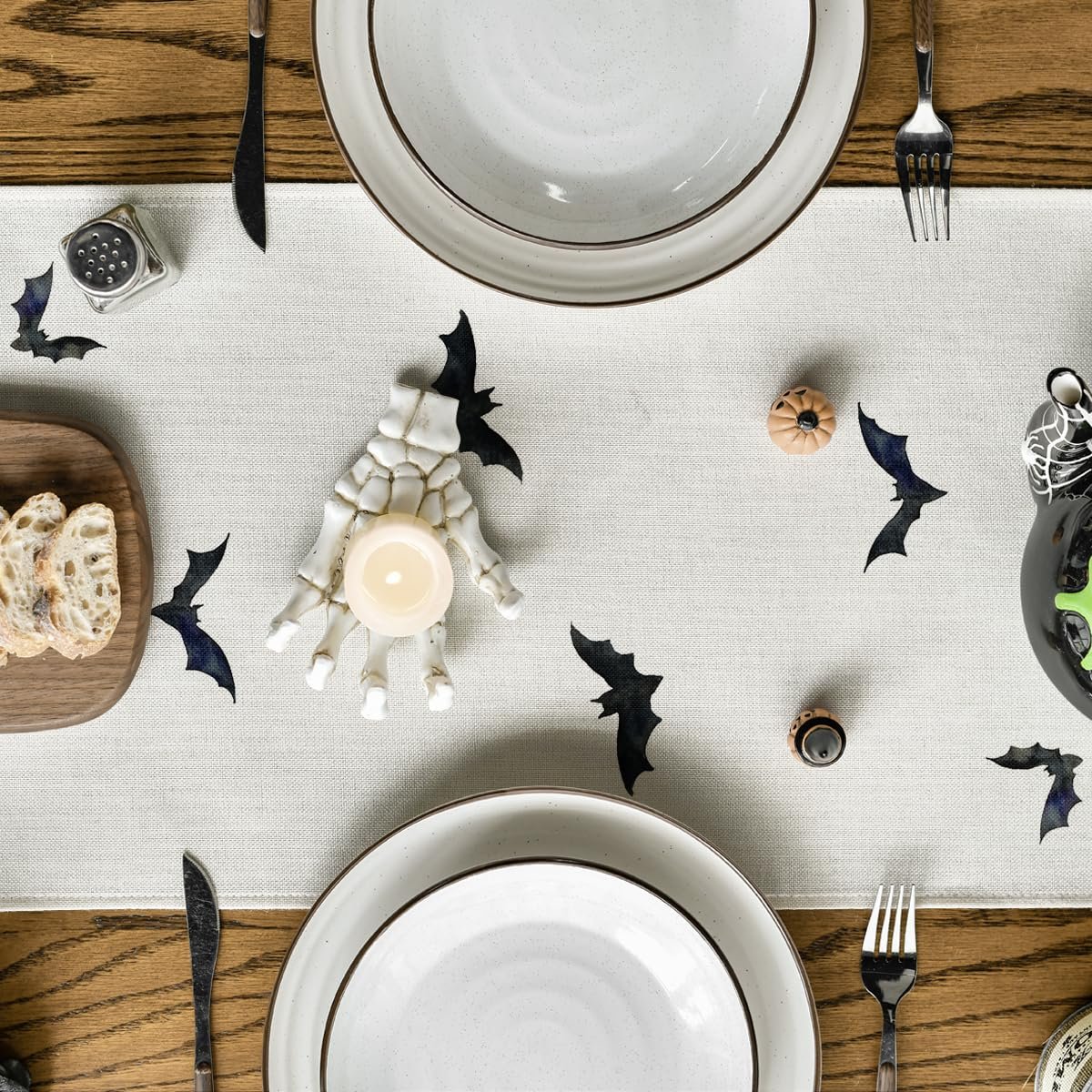 Halloween table setting with a black bat runner, skeleton hand candle holder, plates, and bread.