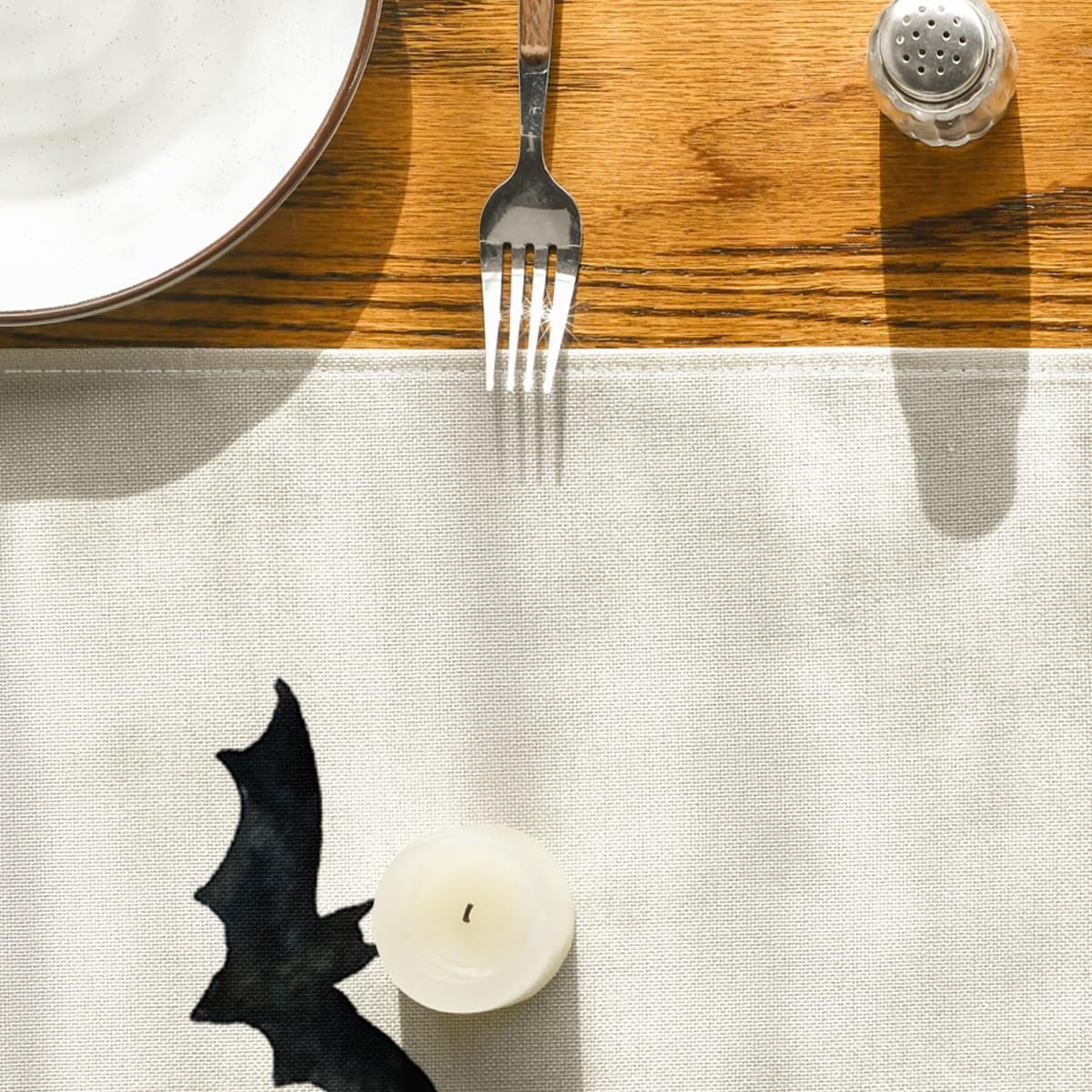 Halloween table runner with black bats and a candle, set with a plate and fork on a wooden table.