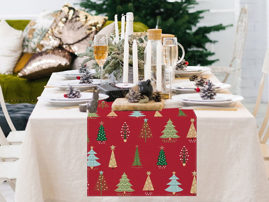 Christmas table runner with red background and green and gold pine trees displayed on a set dining table.