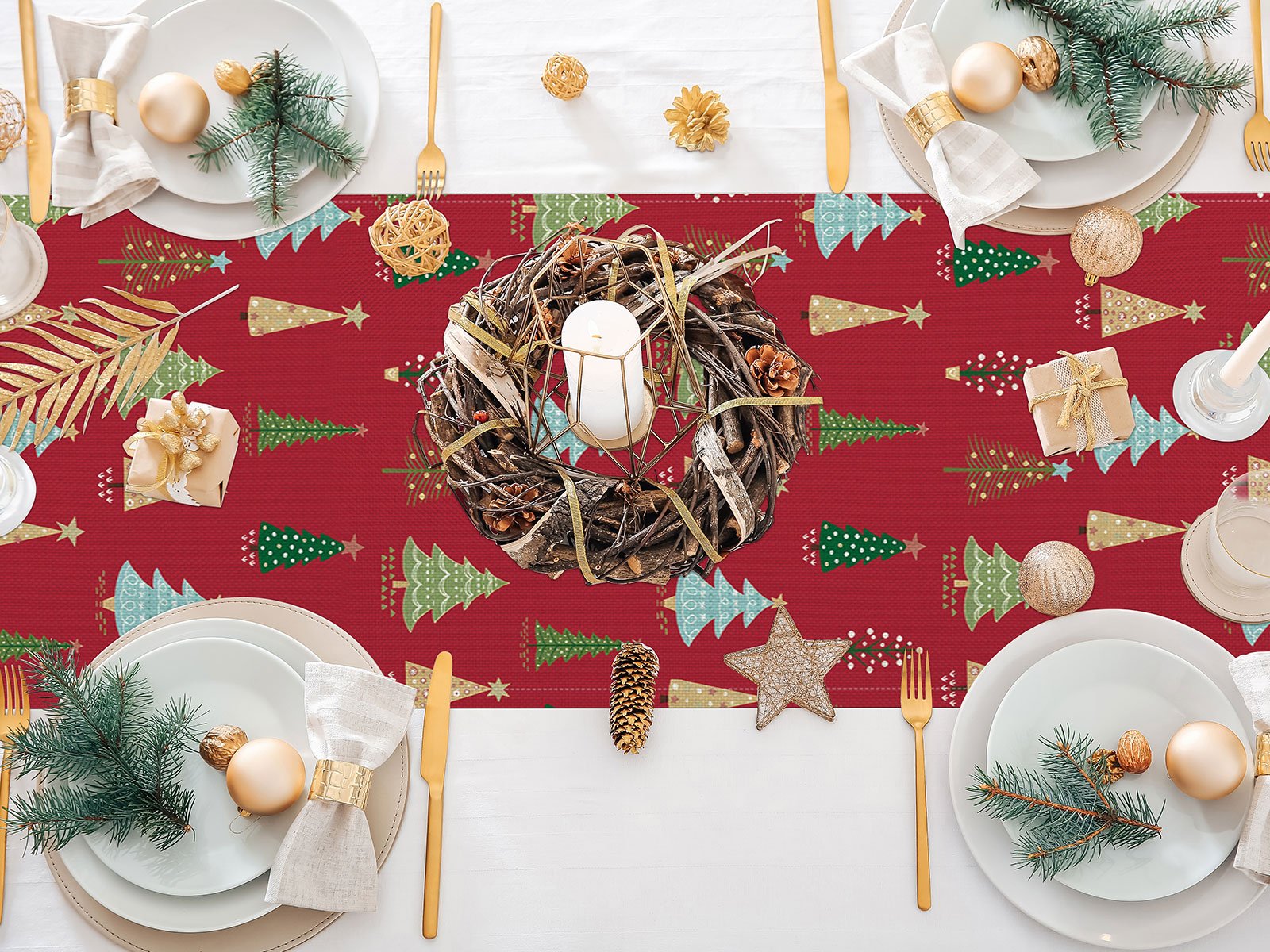 Christmas table runner with red background and green, gold, and blue trees, set with plates, cutlery, and decorations.