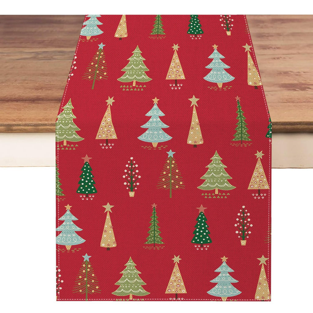 Red Christmas table runner with a pattern of various decorated pine trees, laid on a wooden surface.