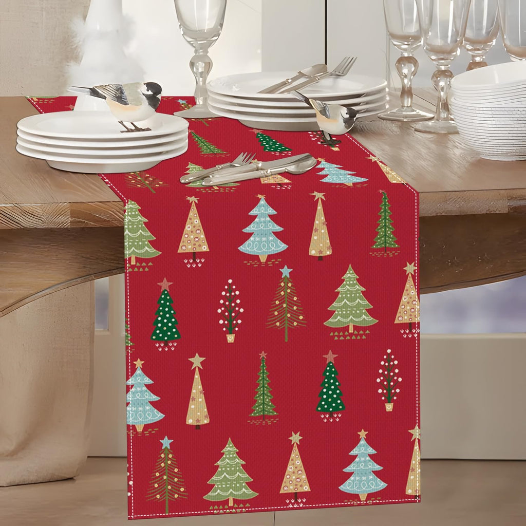 Red Christmas table runner with pine tree pattern, set on a dining table with plates and cutlery.