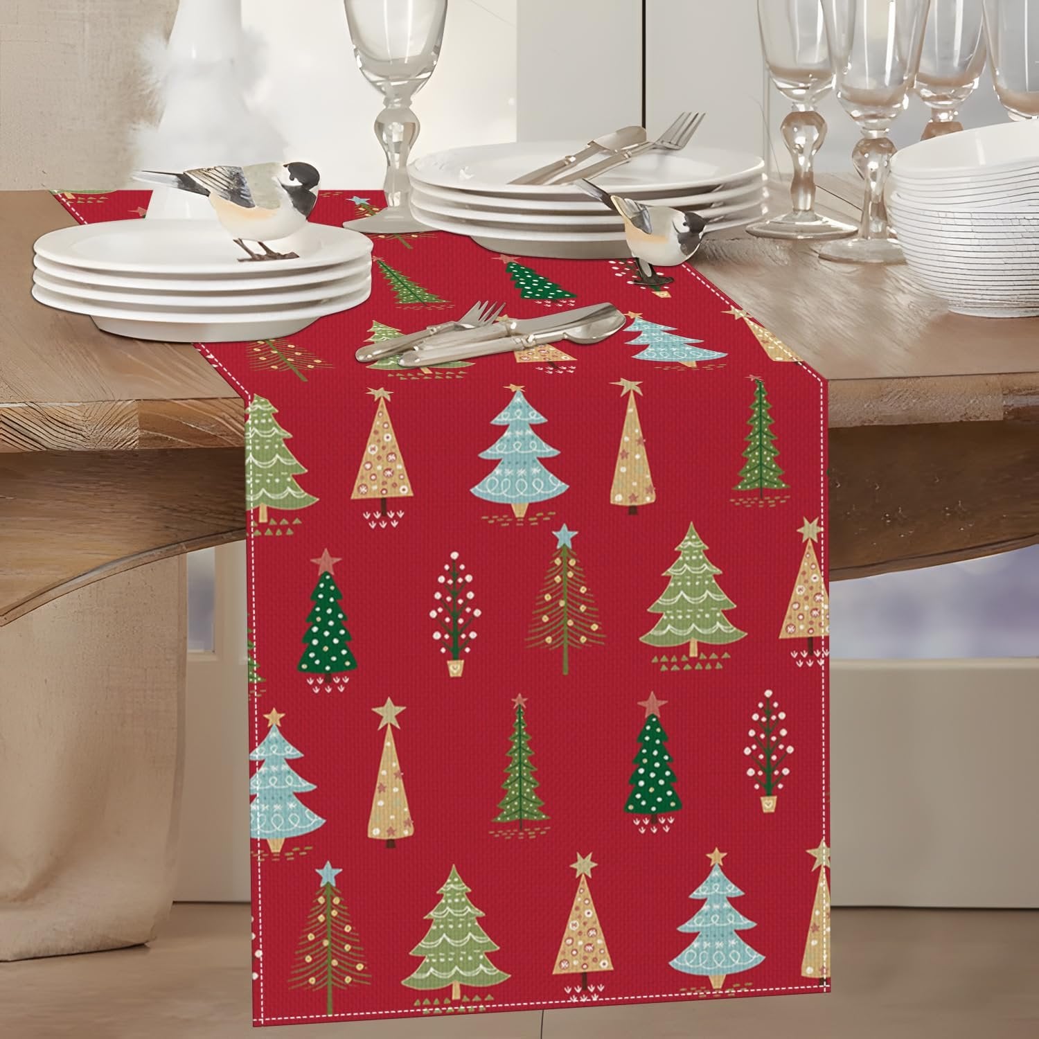 Red Christmas table runner with pine tree pattern, set on a dining table with plates and cutlery.