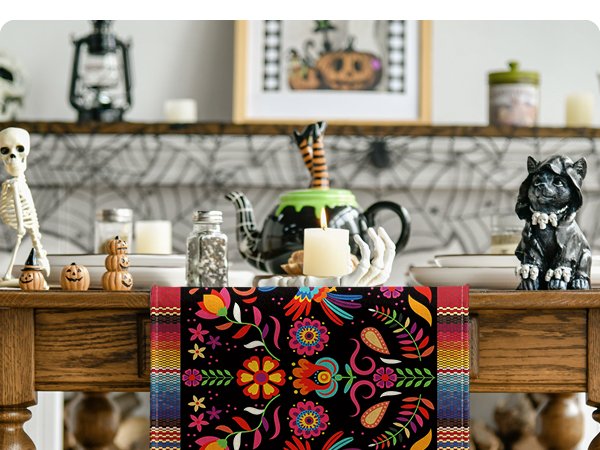 Day of the Dead table runner with colorful floral and paisley patterns on a black background, displayed on a wooden table with Halloween decorations.