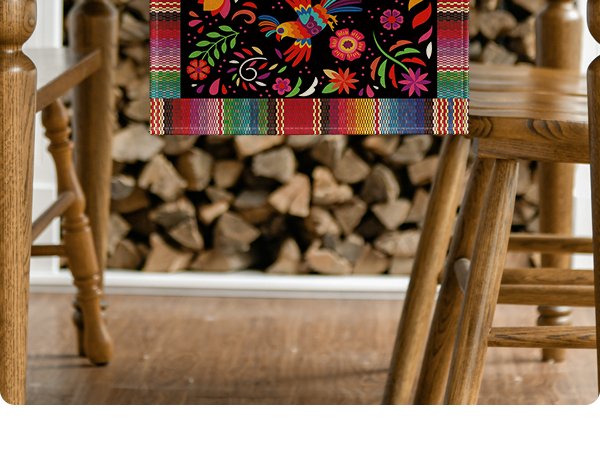 Colorful Day of the Dead serape table runner with floral and bird designs draped over a wooden table.