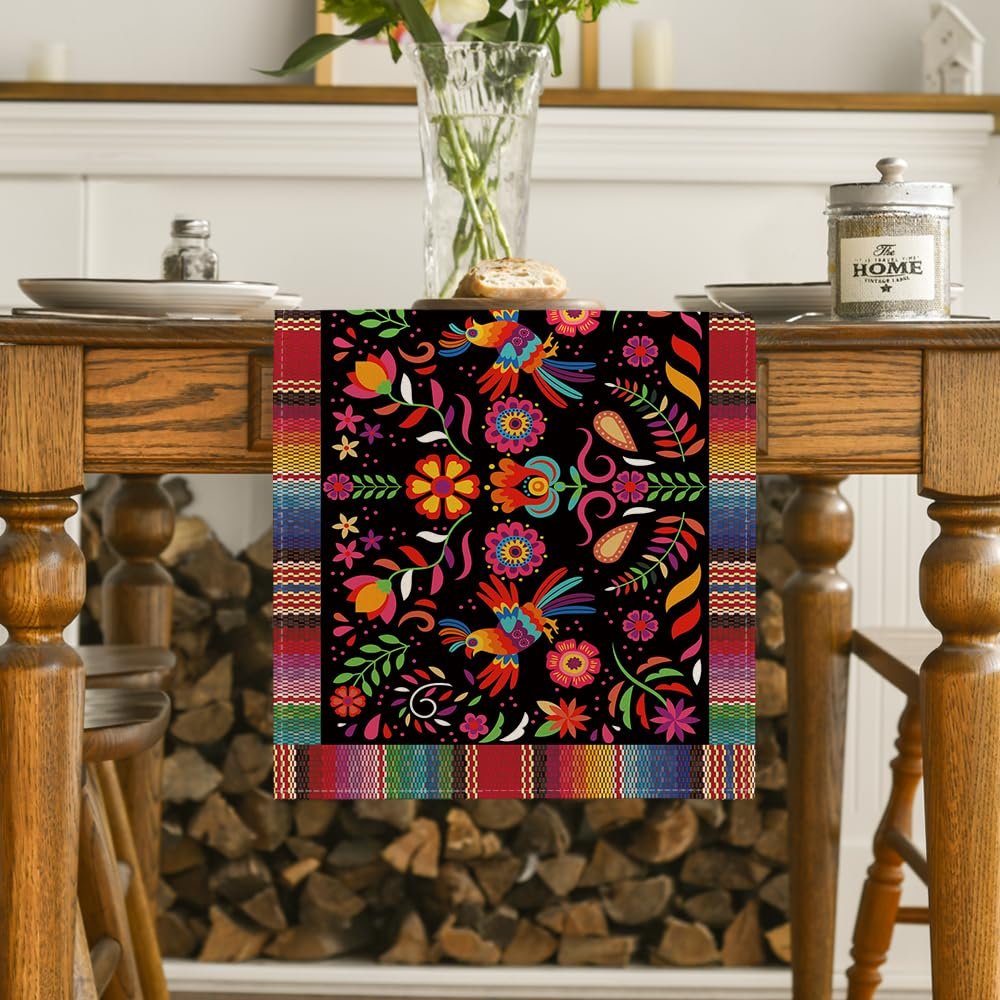 Colorful Mexican fiesta table runner with birds and floral patterns on a black background, laid on a wooden table.