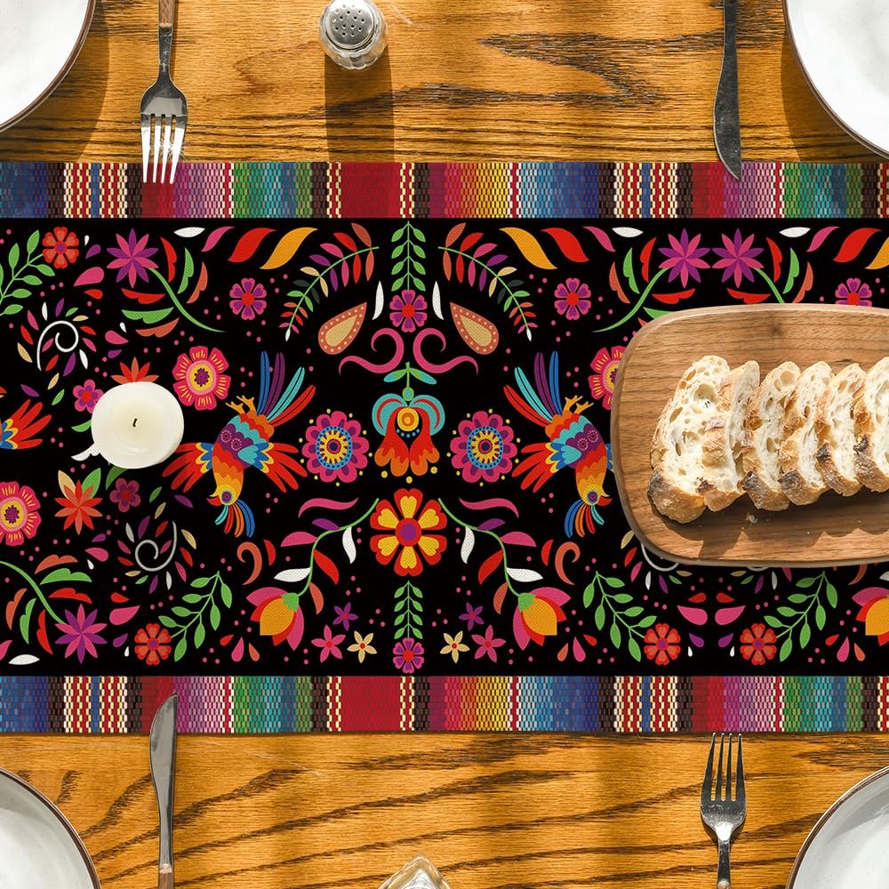 Mexican fiesta table runner with colorful birds and floral patterns on a black background, set on a wooden table with place settings.
