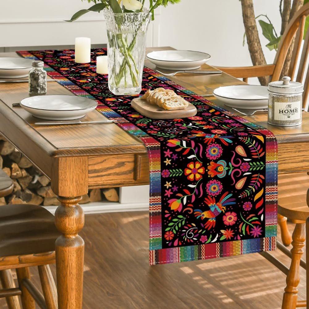 Mexican fiesta table runner with colorful floral and bird patterns on a black background, set on a dining table.