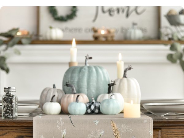 Fall table runner with pumpkin and leaf print on a table with decorative pumpkins and candles