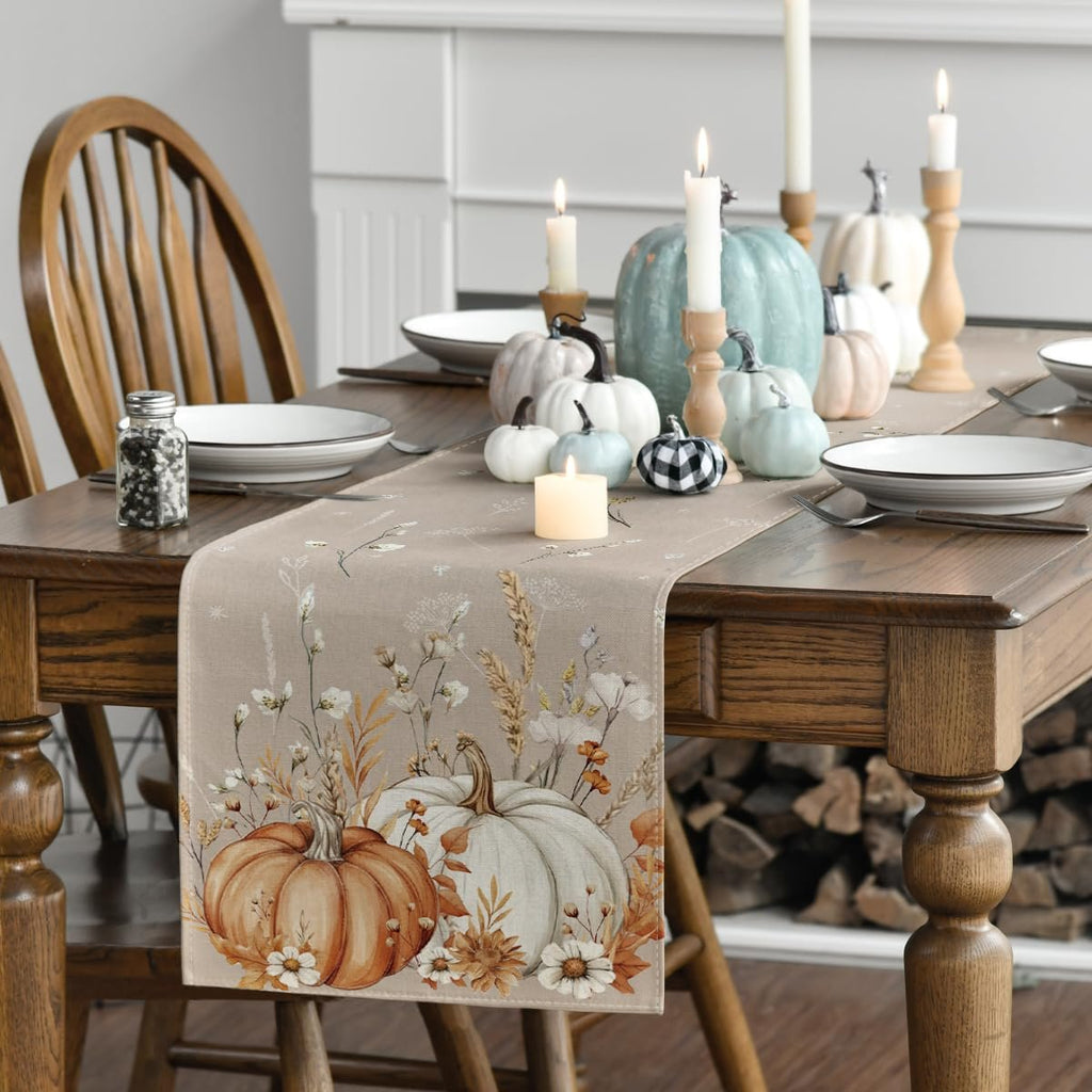 Fall table runner with pumpkins and floral print laid on a wooden dining table with place settings and candles