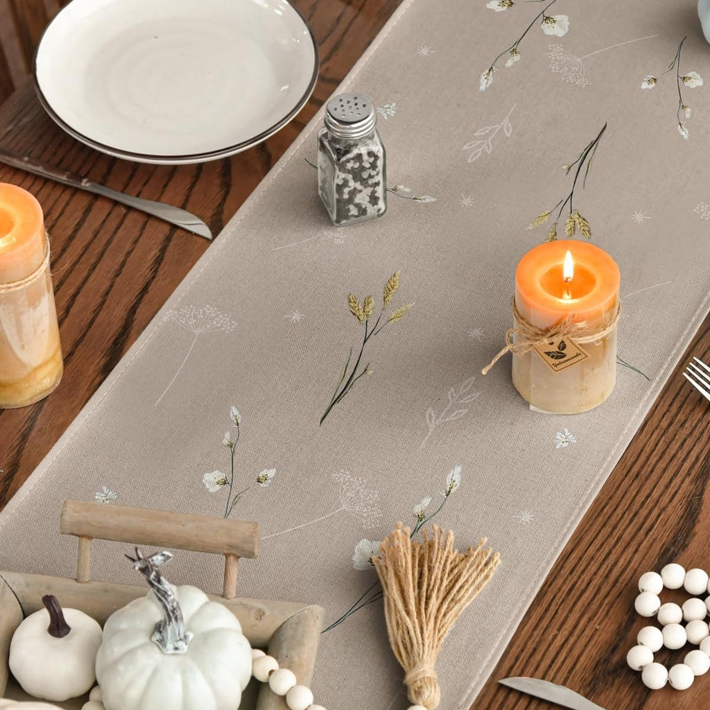 Fall table runner with floral and wheat print, set on a wooden table with candles and pumpkins.