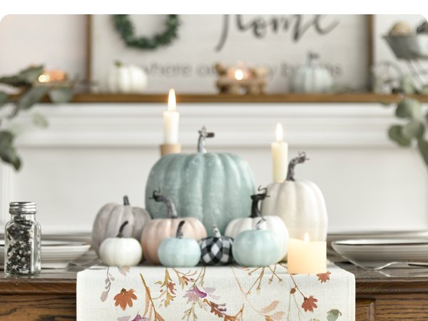 Autumn table runner with floral leaves pattern displayed on a table with pumpkins and candles.