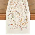 Cream table runner with a watercolor floral and leaf pattern in autumn colors, laid on a wooden table.