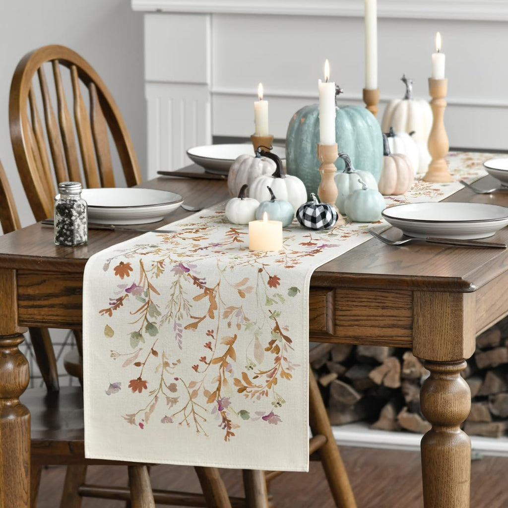 Table runner with floral leaves pattern on a wooden dining table set for fall with pumpkins and candles