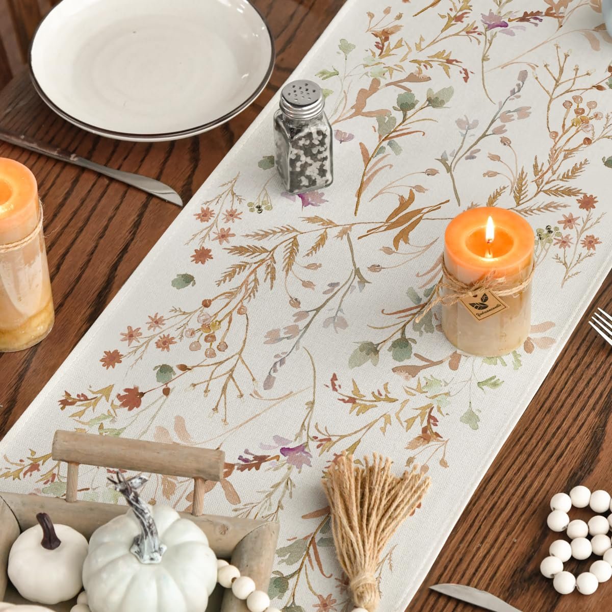 Table runner with floral leaves pattern on a wooden table with candles and pumpkins