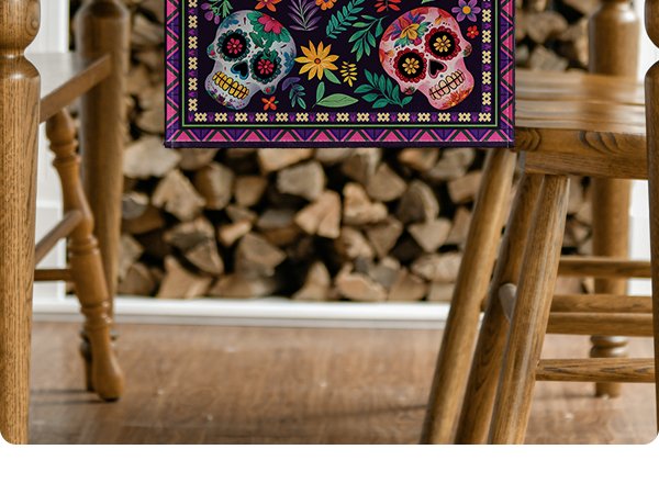 Table runner with sugar skull and floral pattern draped over a wooden table with chairs and firewood in the background.