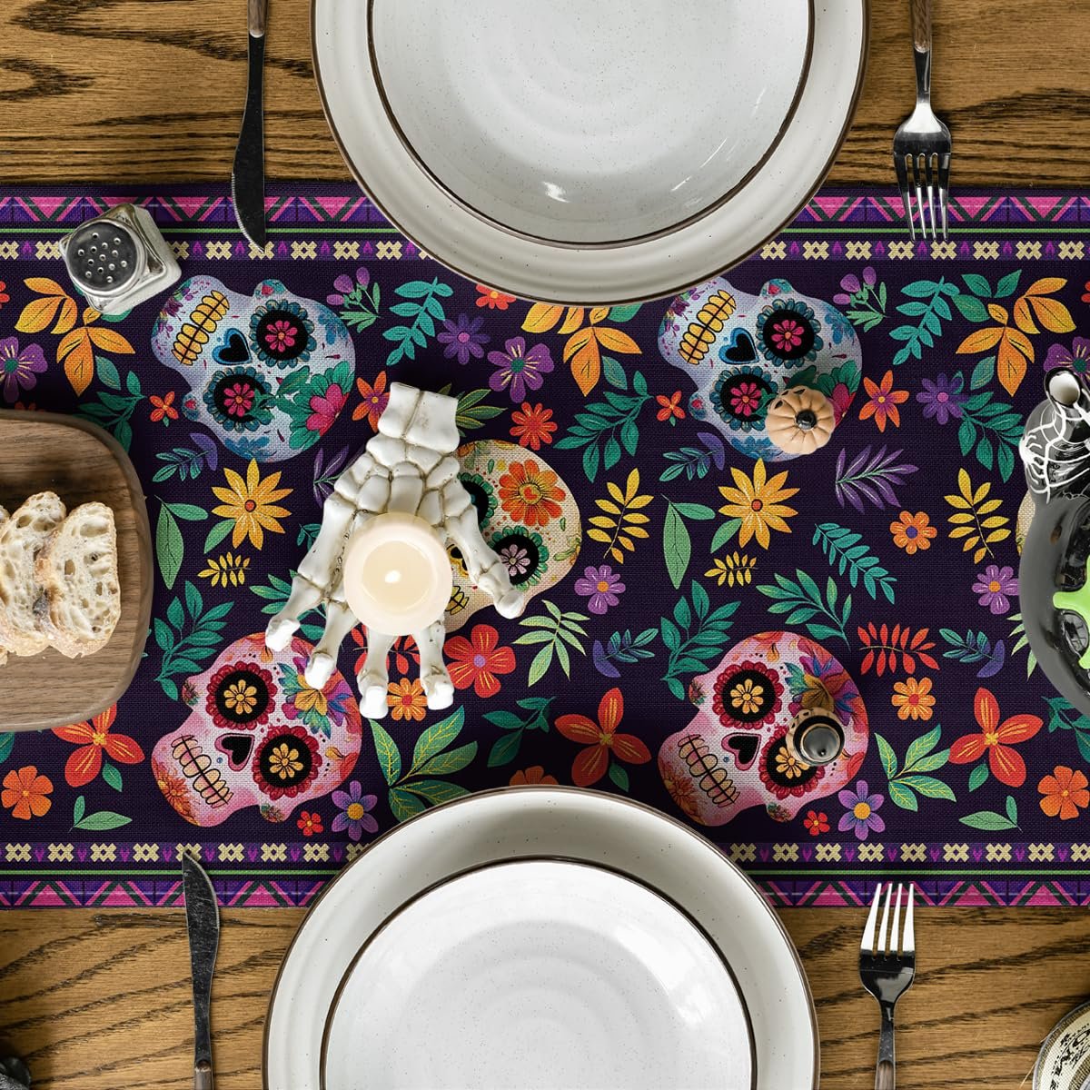 Dia de los Muertos table runner with sugar skulls and floral pattern set on a wooden table with place settings.