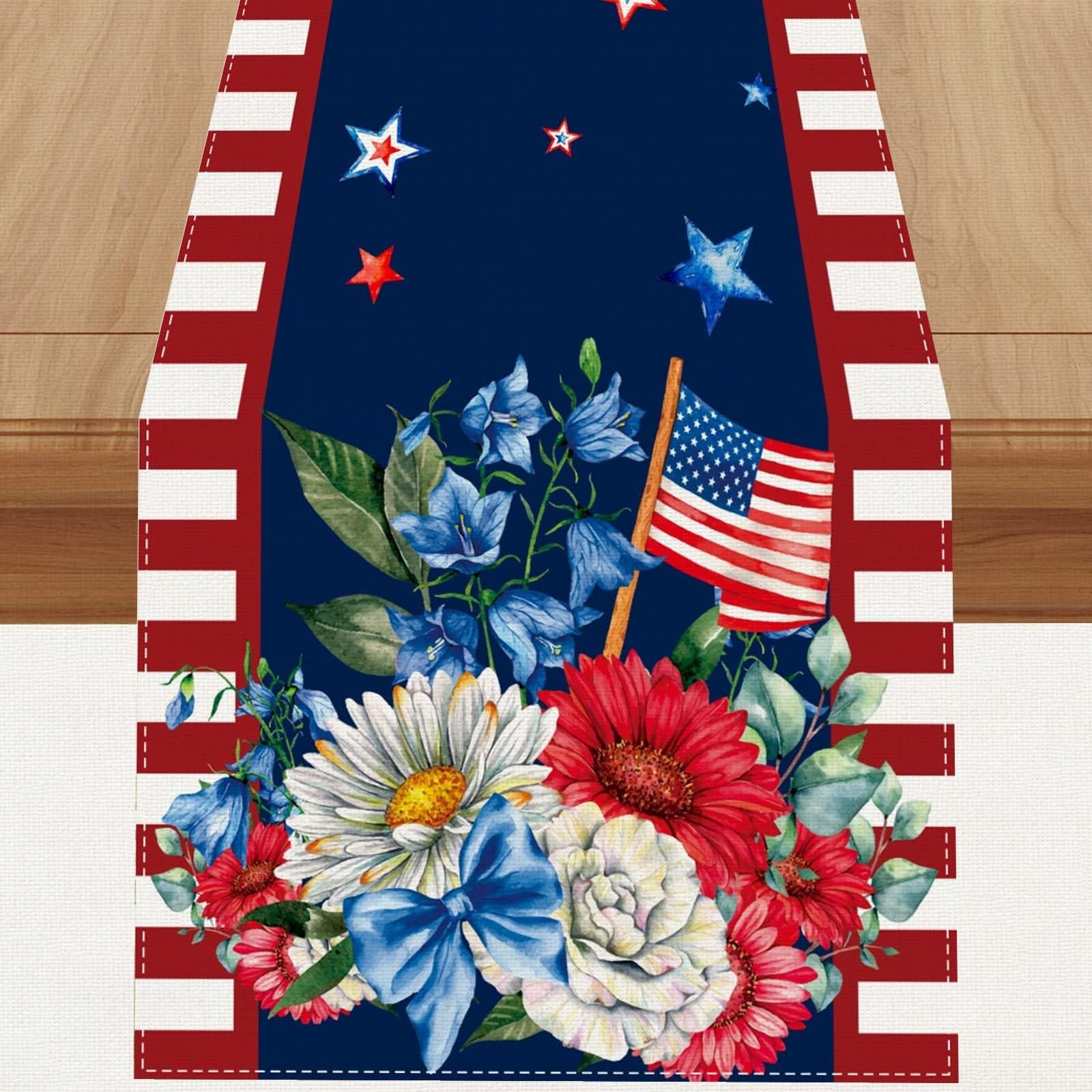 American flag table runner with red and white stripes, blue background, stars, and floral arrangement with red, white, and blue flowers and a blue bow.