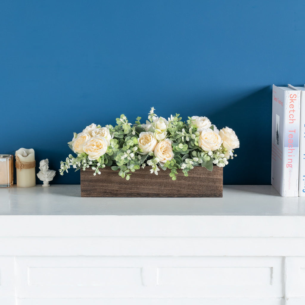 Wooden centerpiece box with artificial yellow roses and eucalyptus on a white shelf with books and candles