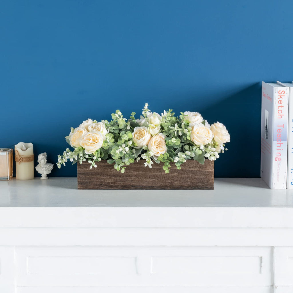 Wooden planter box filled with artificial cream roses and eucalyptus greenery, displayed on a white shelf.