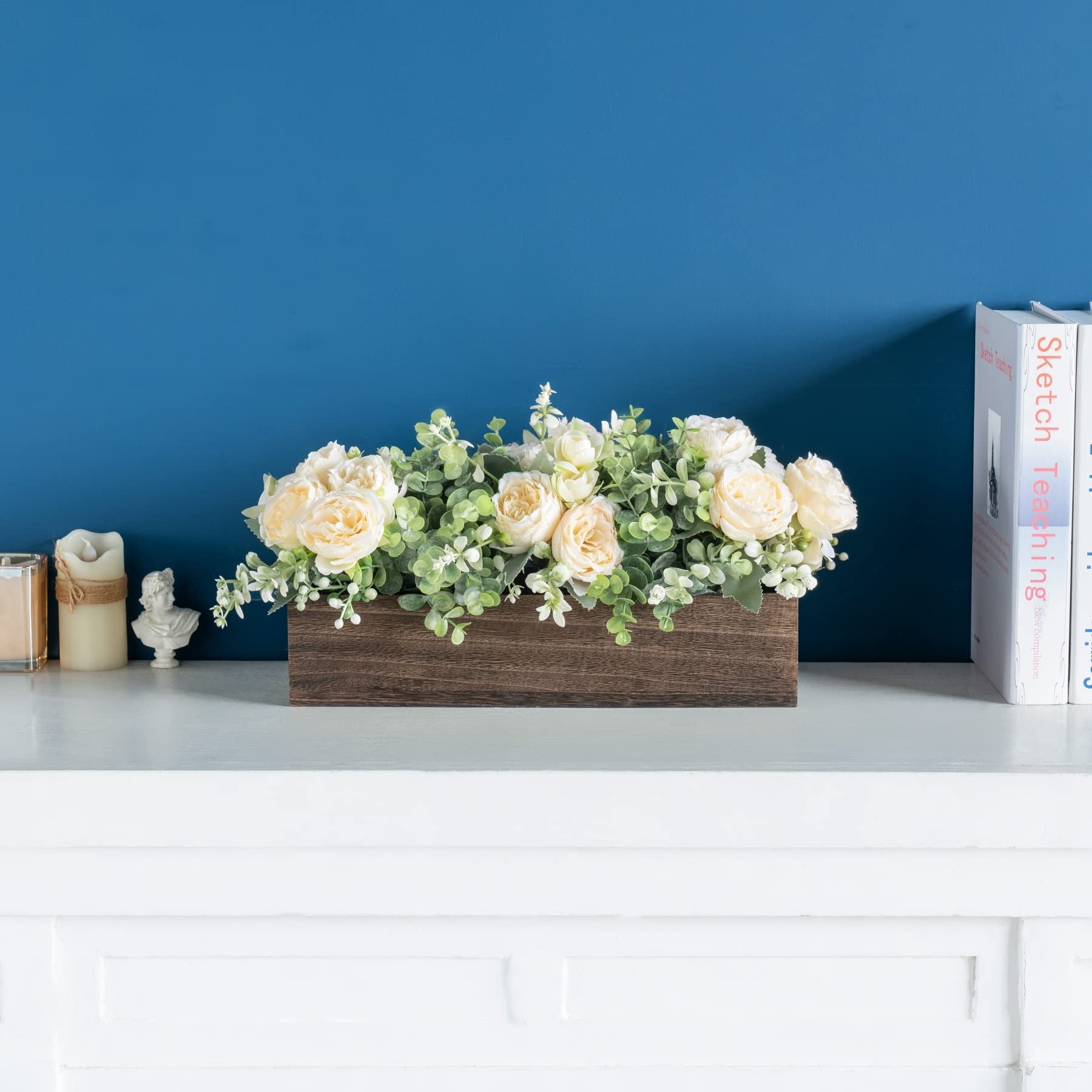 Wooden planter box filled with artificial cream roses and eucalyptus greenery, displayed on a white shelf.