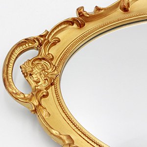 Close-up of an ornate gold oval wall mirror with decorative scrollwork on a white background.