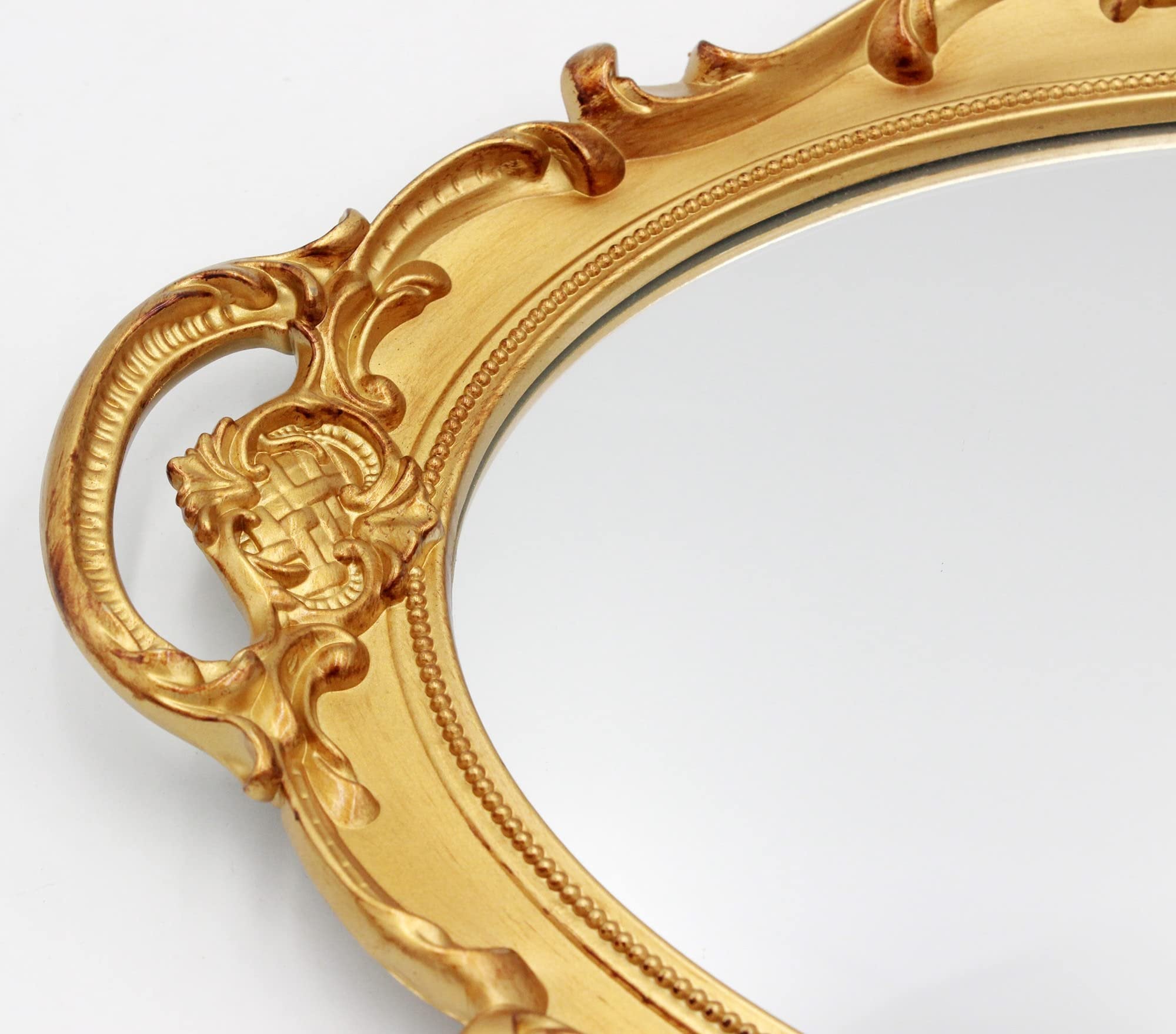 Close-up of an ornate gold oval wall mirror frame with decorative scrollwork and beaded trim.